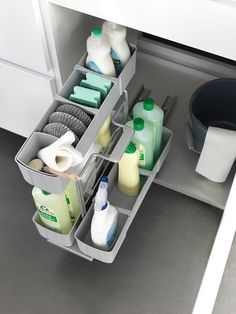 an open cabinet with cleaning products and toiletries in the bottom drawer, next to a trash can