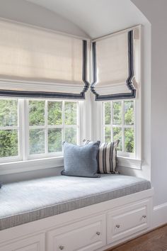 a window seat with pillows on it in front of two windows, one is white and the other is blue