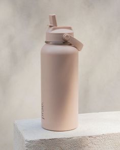 a pink water bottle sitting on top of a cement block next to a white wall