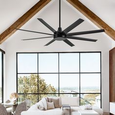 a living room filled with furniture and a ceiling fan in front of large windows that look out onto the countryside