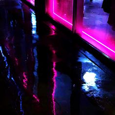 a person walking down a street at night with an umbrella on the wet ground and neon lights behind them