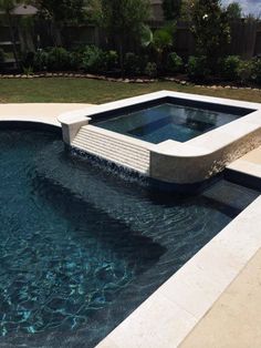 an outdoor swimming pool with water running from the bottom to the top, surrounded by grass and trees