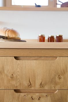 bread and jams sit on top of a wooden dresser in a kitchen with white walls