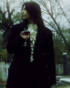 a man in a suit and tie holding a glass of wine standing next to a tree