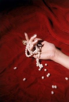 a woman's hand with pearls and beads on her wrist, resting on a red sheet