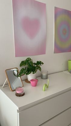 two paintings on the wall above a dresser with plants and other items sitting on it