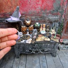 a hand is holding up a miniature witch's hat over a table full of items