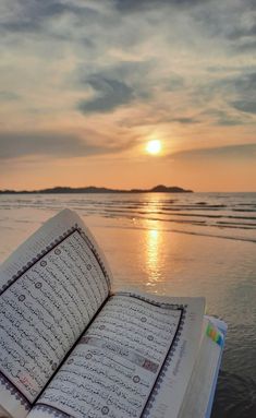 an open book sitting on top of a beach next to the ocean