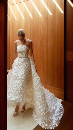 a woman standing in front of a wooden wall wearing a white dress with flowers on it