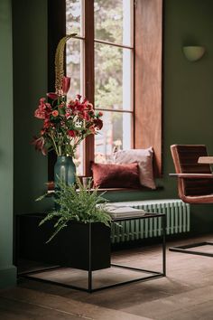 a vase filled with red flowers sitting on top of a table next to a window