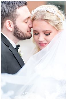 a bride and groom pose for a wedding photo in their tuxedo, veil draped over their heads