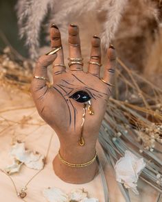 a hand with an eye painted on it next to dried flowers and branches in the background