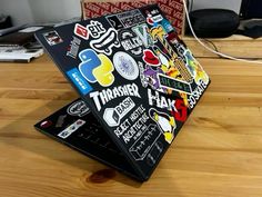 a laptop covered in stickers sitting on top of a wooden table