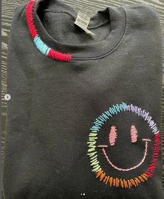 a t - shirt with a smiley face drawn on it's chest and colorful beads around the neck