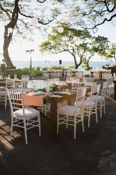 an outdoor dining area with white chairs and tables set up on the side of the beach