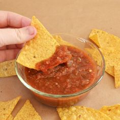 a person dipping salsa into tortilla chips