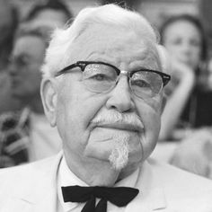 an old man wearing glasses and a suit with a bow tie in front of people