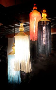 three lamps with fringes hanging from them in a dark room, one is orange and the other is blue