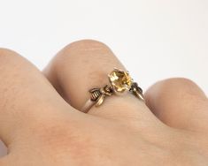 a woman's hand holding a ring with a yellow diamond in the middle and leaves on it