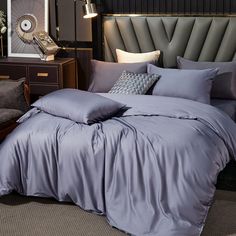 a bed with grey sheets and pillows in a dark room next to a gray chair