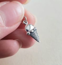 a hand holding a silver charm with an ice cream cone on it's end