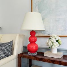 a red lamp sitting on top of a wooden table next to a white couch and chair