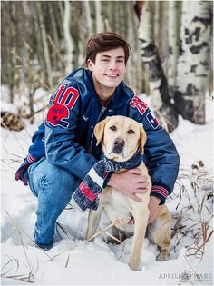 a young man kneeling in the snow with his dog wearing a blue jacket and scarf