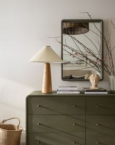 a green dresser with a lamp on top and a painting above it in the corner