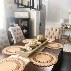 a dining room table with place mats and pumpkins on the centerpiece in front of it