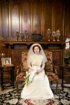 a woman in a wedding dress sitting on a chair next to a fireplace with flowers