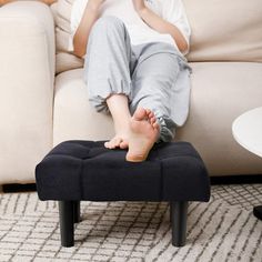 a woman sitting on top of a black ottoman in front of a white coffee table