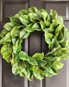 a green wreath is hanging on the front door, with leaves around it's edges