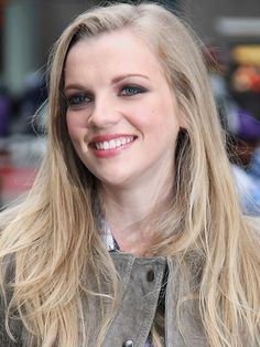 a woman with long blonde hair and blue eyes smiles at the camera while wearing a leather jacket