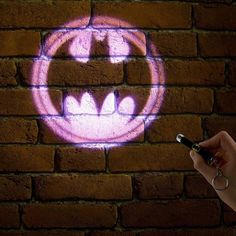 a brick wall with a drawing of a batman symbol on it and a hand holding a pen