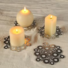 four lit candles sitting on top of a white cloth covered tablecloth with black circles around them