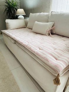 a white couch with pink and white pillows on top of it next to a potted plant