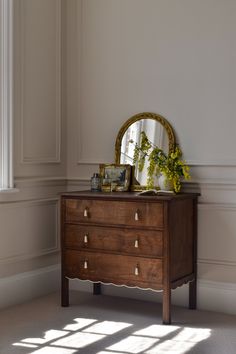 a dresser with a mirror and flowers on it in a room that has white walls