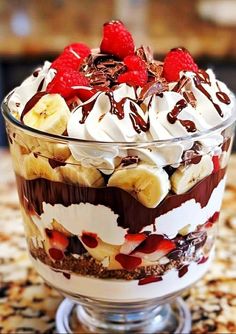 a dessert in a glass dish with chocolate, banana and raspberries on top