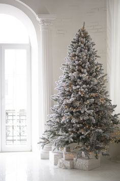 a white christmas tree with presents under it in front of an arched doorway and window