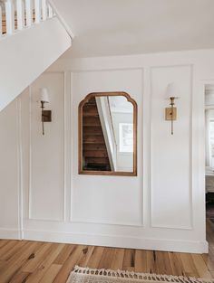 an empty room with white walls and wood flooring in the foreground is a mirror on the wall