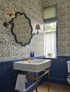 a bathroom with blue and white wallpaper, gold fixtures and a large mirror above the sink