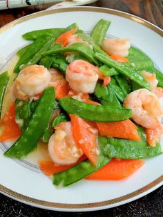 a white plate topped with shrimp and veggies on top of a wooden table