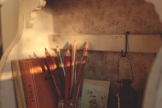 there are many different colored pencils in a glass on the shelf next to an old book