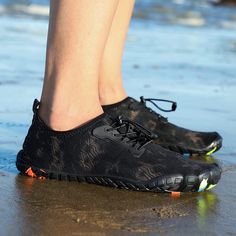 a close up of a person's feet wearing black shoes on the sand and water