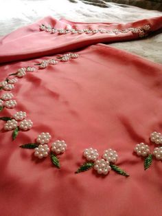 a pink dress with flowers and pearls on the neckline is laying on a bed