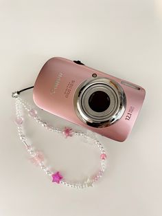 a pink digital camera sitting on top of a white table next to a beaded necklace