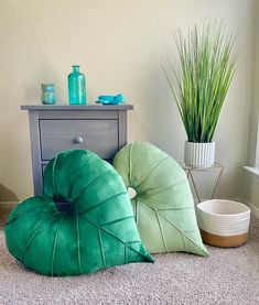 three green pillows sitting on top of a carpet next to a dresser and potted plant