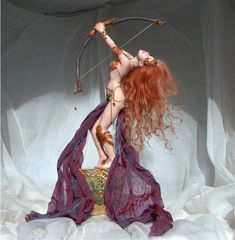 a woman with red hair is holding a bow and arrow in her hand while standing on a white sheet