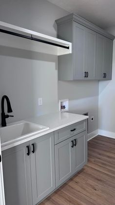 a kitchen with gray cabinets and white counter tops in an empty room that has wood flooring