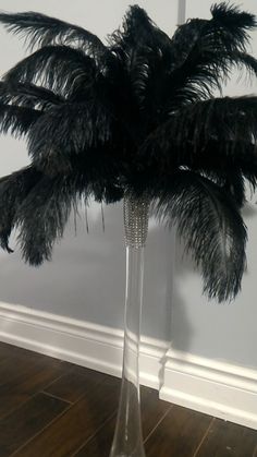 a tall glass vase filled with feathers on top of a wooden floor next to a wall